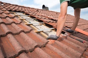 man at uncovered roof, replaces broken roof shingles with new ones