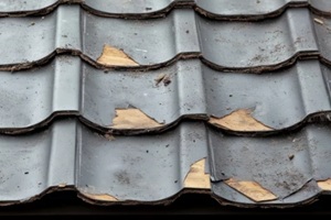 close-up view of a weathered and damaged roof covered with metal tiles showing signs of wear and tear from weather